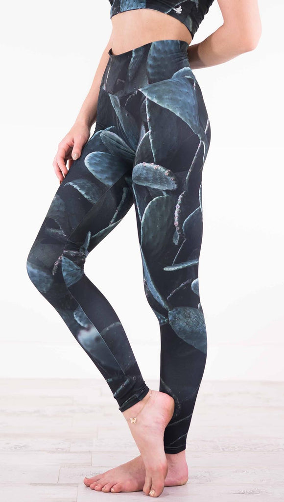 Left view of model wearing black athleisure leggings with dark green cacti plants throughout