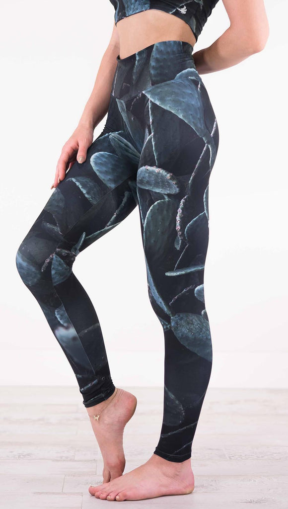 Left view of model wearing black athleisure leggings with dark green cacti plants throughout