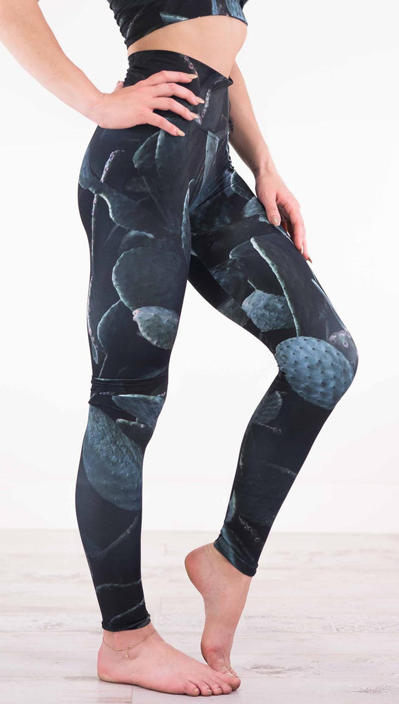 Right view of model wearing black athleisure leggings with dark green cacti plants throughout