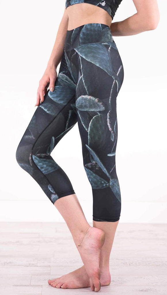 Left view of model wearing black capri leggings with dark green cacti plants throughout