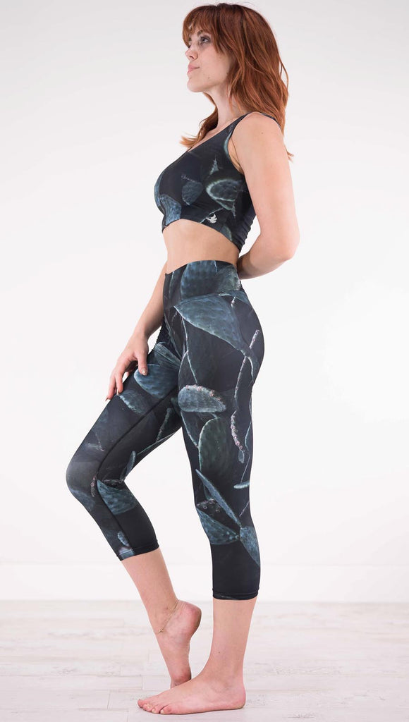 Left view of model wearing black capri leggings with dark green cacti plants throughout