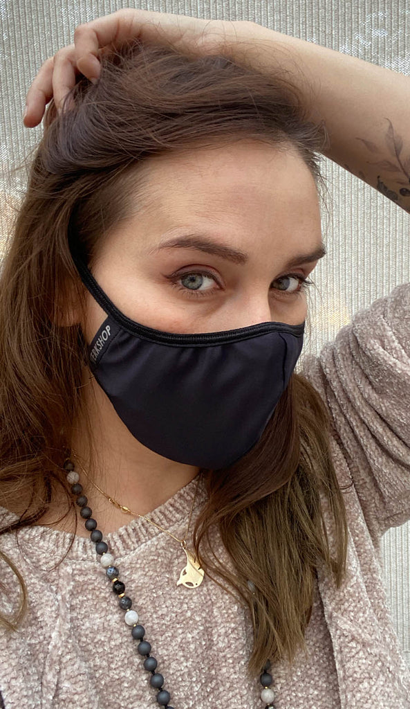 Girl wearing black face mask with silver trim logo and adjustable ear loops