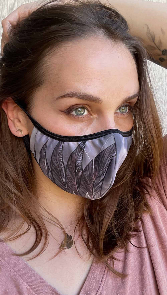 Girl wearing adjustable face mask with purpler thunderbird wings on the right cheek and cloudy storm clouds on left cheek 