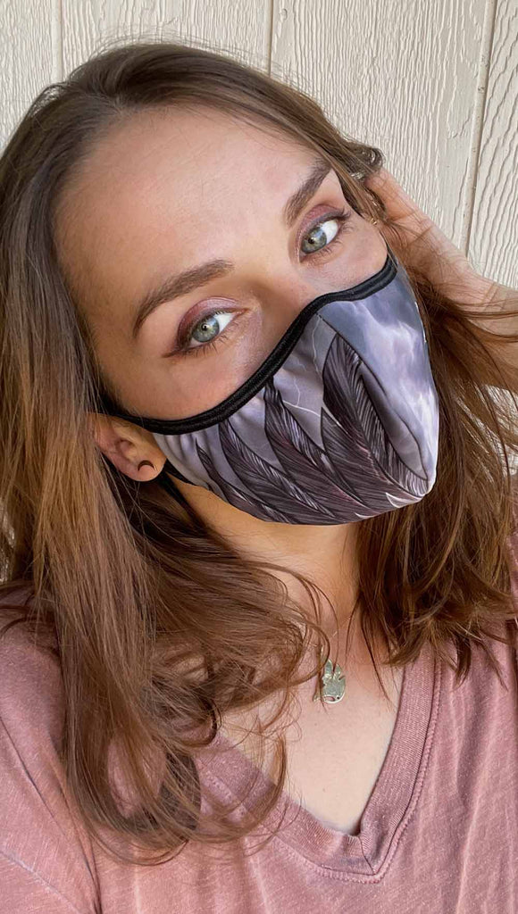 Girl wearing adjustable face mask with purpler thunderbird wings on the right cheek and cloudy storm clouds on left cheek 