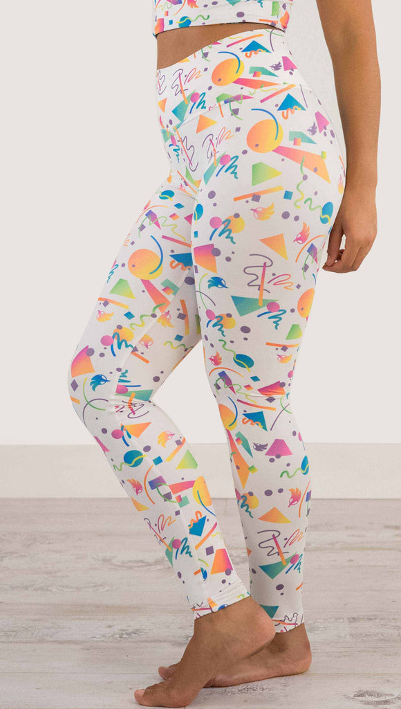 Waist down view of model wearing WERKSHOP white confetti athleisure leggings. The artwork on the leggings shows multi-colored circles, scribbles and triangles over a white background.